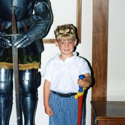 Young Ben holding a toy sword standing next to a suit of armour
